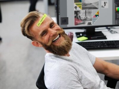 Happy Employee at this desk with a sticky note on his forehead that says "Be Happy"