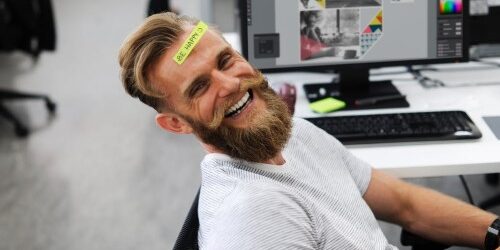 Happy Employee at this desk with a sticky note on his forehead that says "Be Happy"